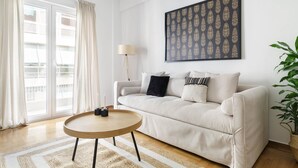 A modern living room with a beige sofa, a round wooden coffee table, and a large framed artwork on the wall. - Urban 2BD Apartment in Koukaki (Athens)