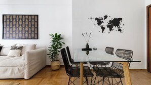 A modern living room with a glass dining table, black wicker chairs, a white sofa, and a large world map on the wall. - Urban 2BD Apartment in Koukaki (Athens)