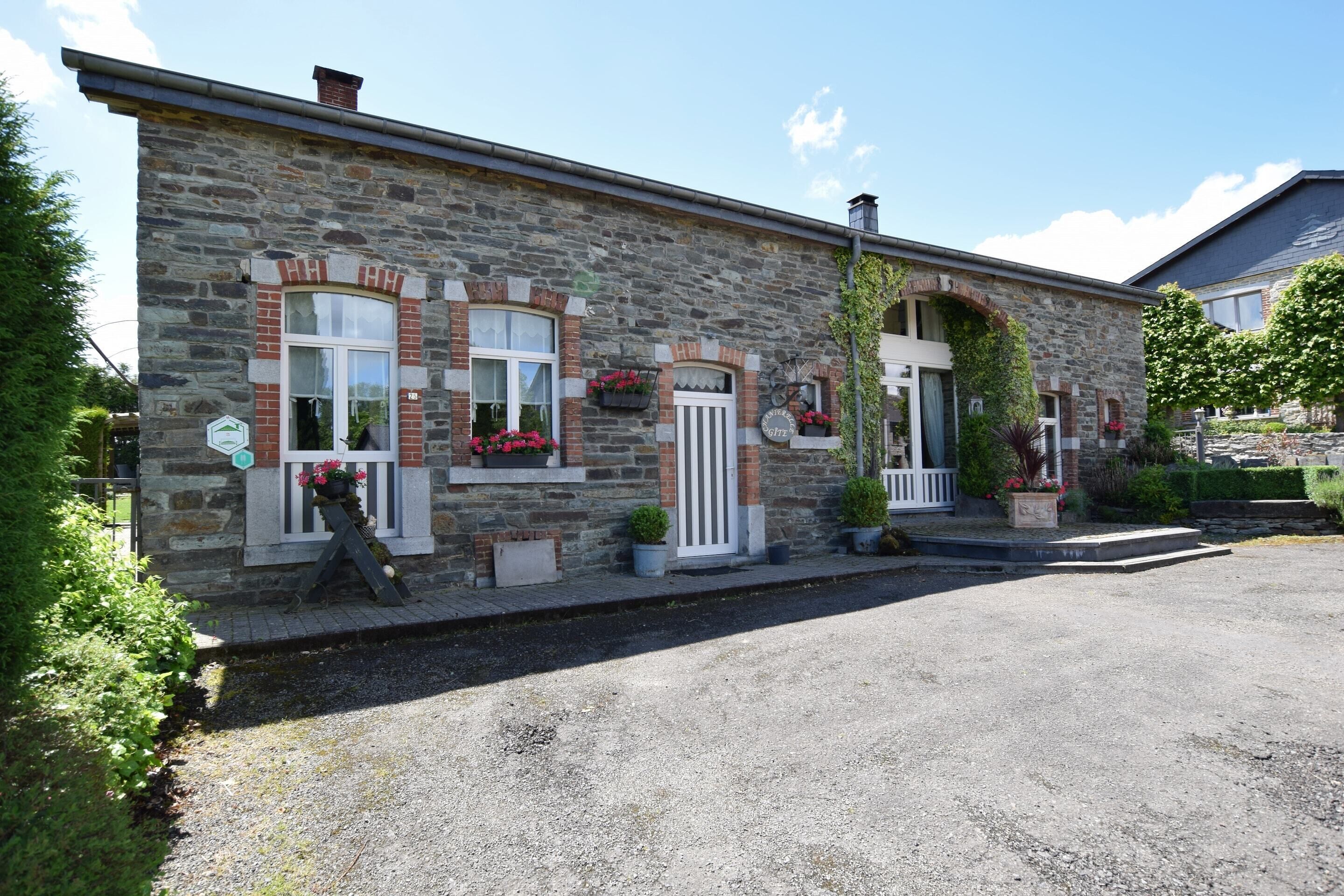 A stone building with a white door and windows, a small porch, and potted plants.