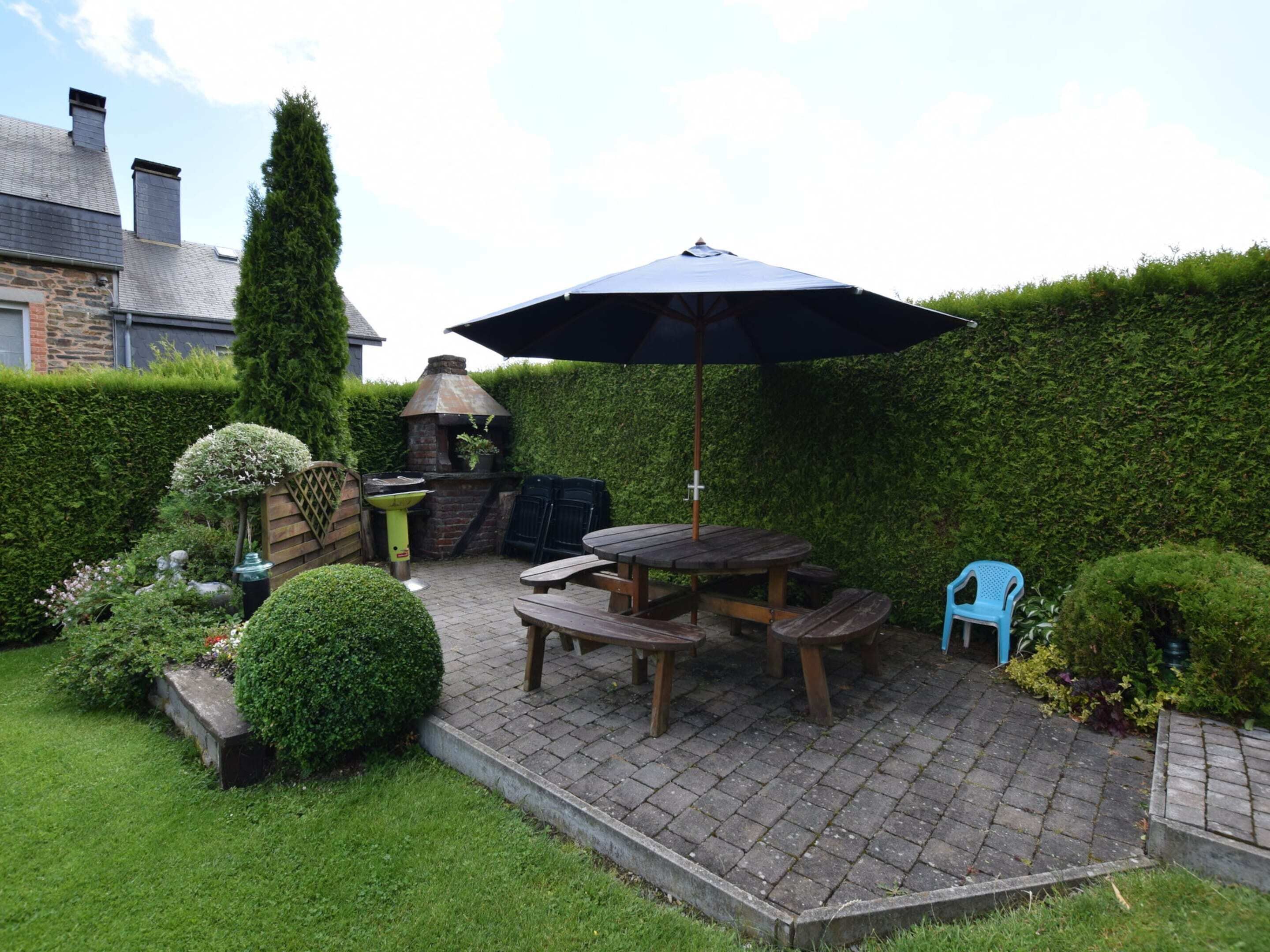 Un'area patio con pavimento in mattoni, tavolo e panche in legno, un barbecue e una sedia blu.