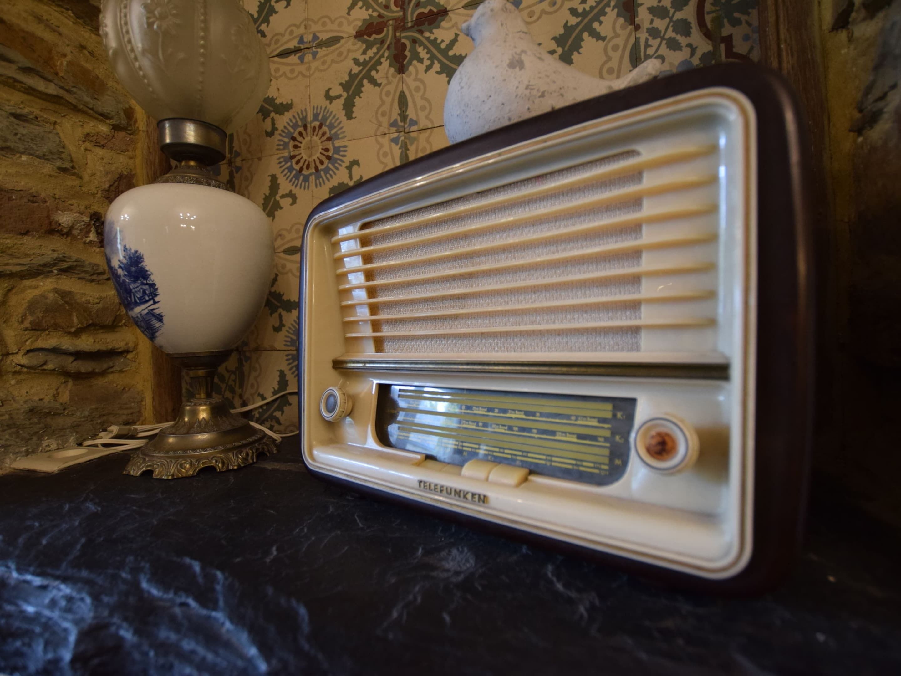 Ein altes Radio mit Drehknopf und Tasten, platziert auf einer dunklen Fläche vor einer Wand mit Muster.