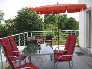 An outdoor patio area with a glass table, red chairs, and a red umbrella. - Elevated Apartment in Bad Wildungen With Garden (Bad Wildungen)
