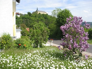 Un jardin agrémenté de fleurs blanches et violettes, une statue et un bâtiment avec une tour en arrière-plan.