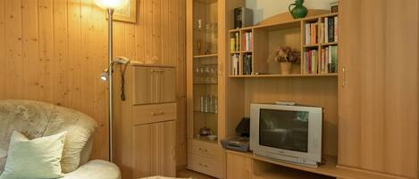 Ein gemütliches Zimmer mit einem Bett, einem Fernseher, Holzschränken und einem Bücherregal.