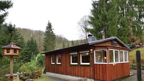 Eine Holzhütte mit geneigtem Dach, großen Fenstern und einer kleinen Veranda.