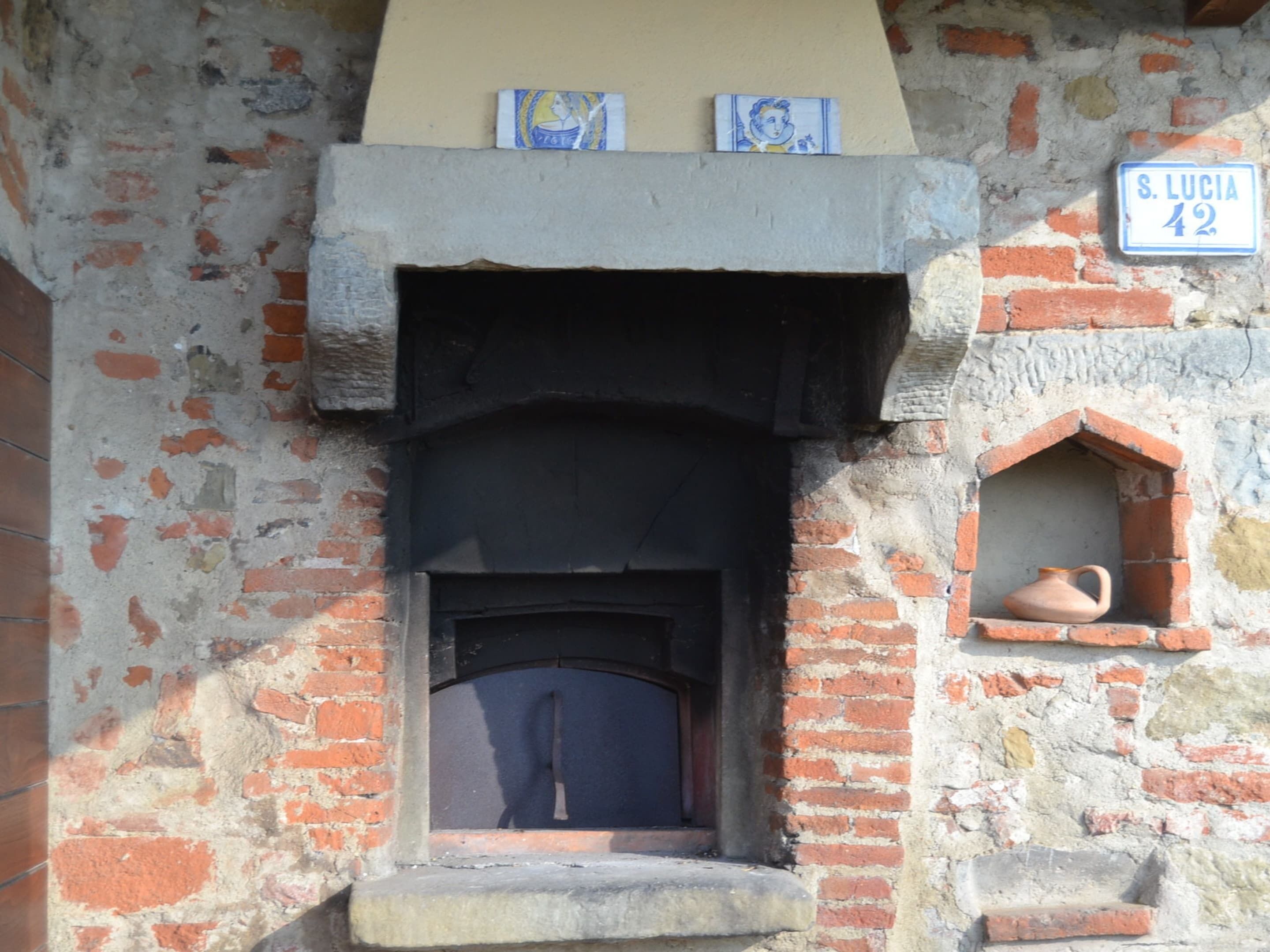 Une façade rustique avec un mur en briques, une petite fenêtre ornée d’un pot en terre cuite et une enseigne indiquant « S. Lucia 42 ».