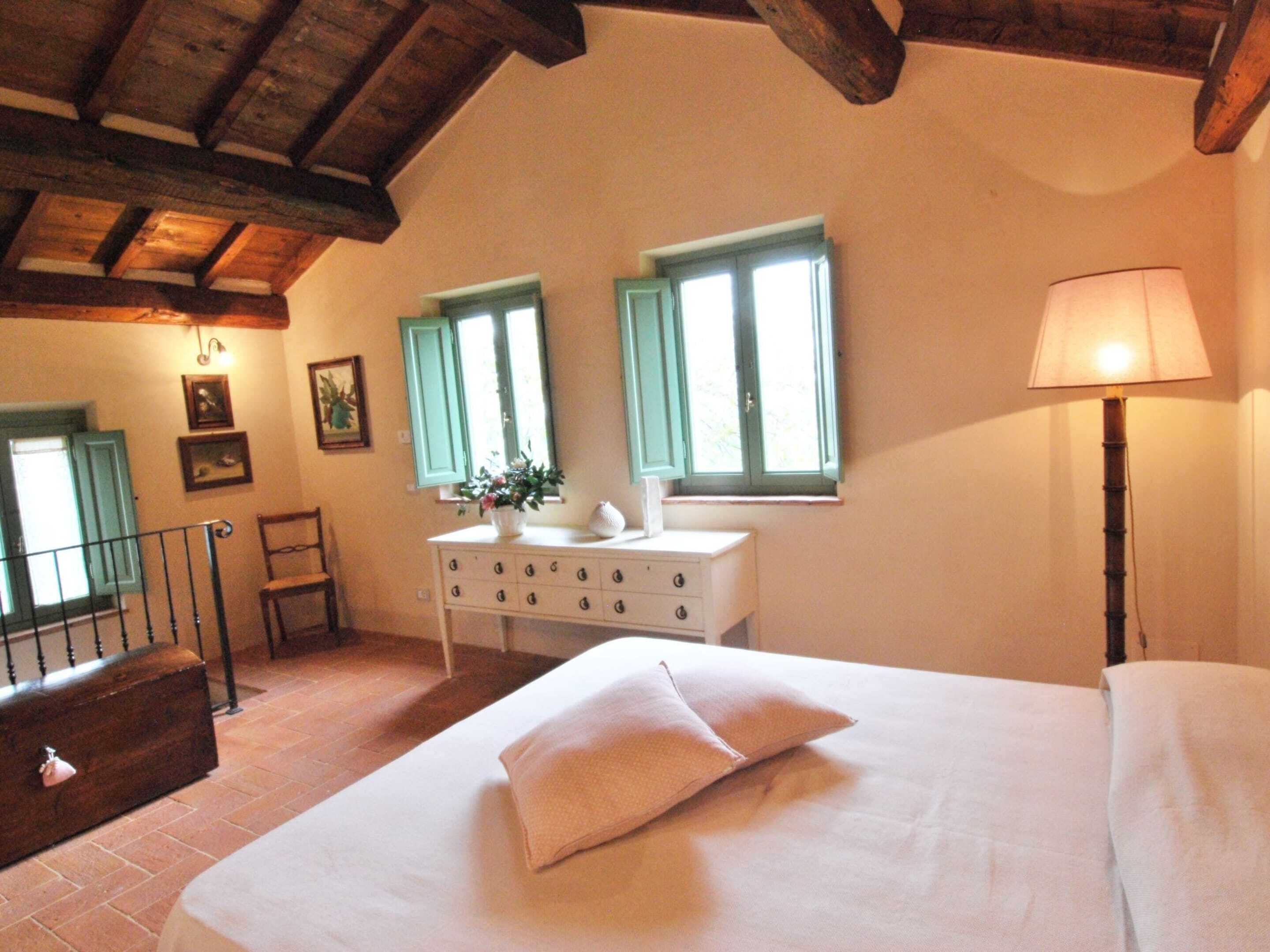 A bedroom with a bed, a dresser, a lamp, and two windows with shutters.