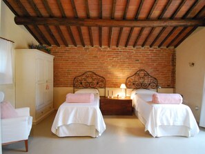 A room with two beds, a wardrobe, and a brick wall. - Cottage in Val di Chiana (Castiglion Fiorentino)