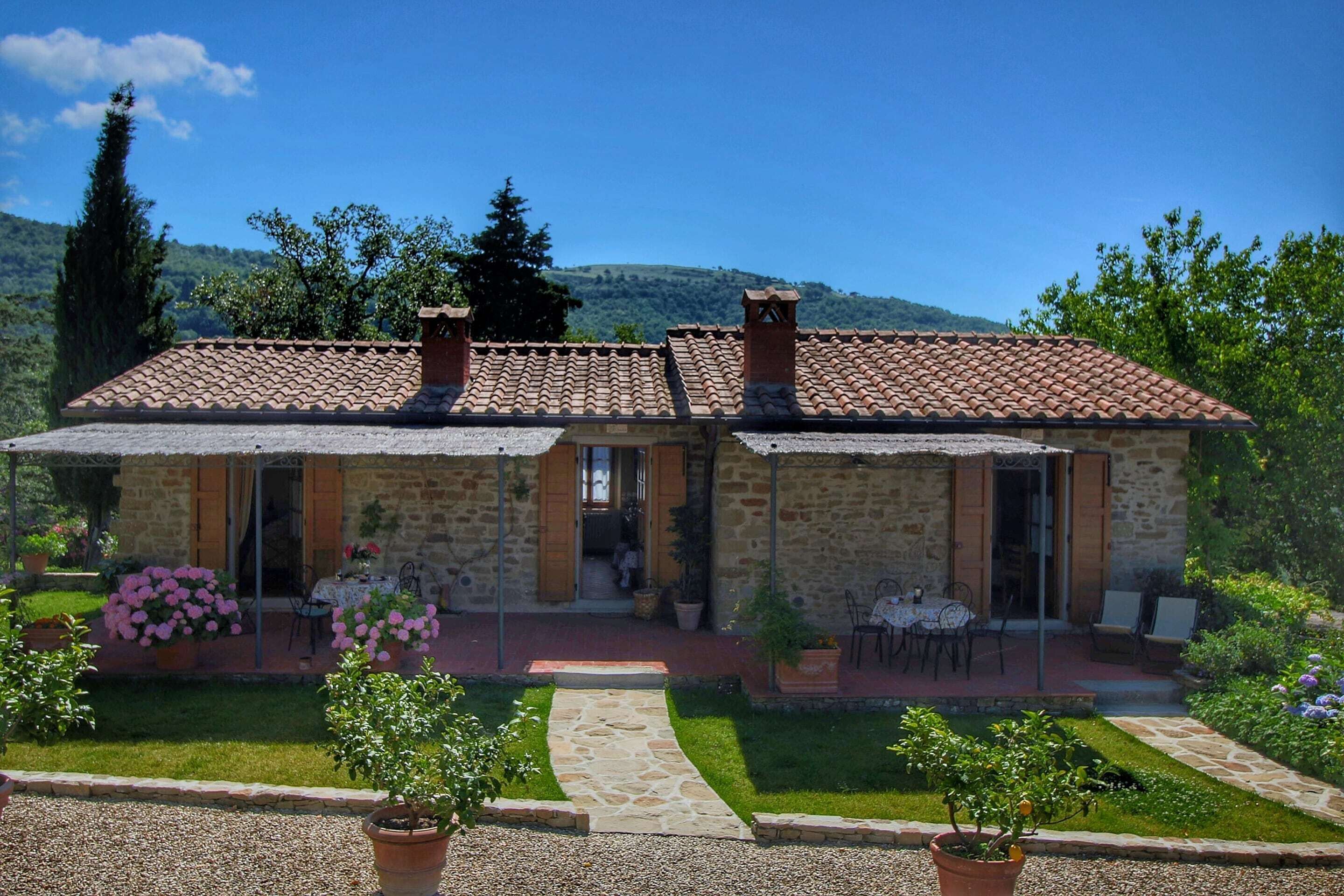 A stone building with a tiled roof, a paved patio, and a garden with potted plants.