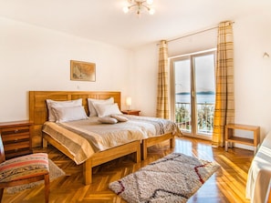 A bedroom with a wooden bed, a nightstand, a chair, a rug, and a view of the sea through a large window. - Magnificent Villa in Supetar With Swimming Pool (Supetar)