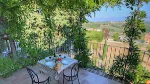 An outdoor dining area with a table set for two, surrounded by greenery and overlooking a scenic landscape. - Farmhouse Bliss With Pool, Wine and Tails (Gualdo Cattaneo)