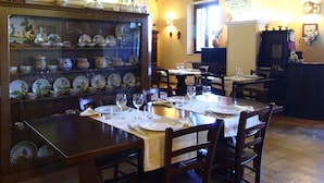 A dining area with a brick archway, wooden tables set with plates and glasses, and a display of decorative plates on shelves. - Farmhouse Bliss With Pool, Wine and Tails (Gualdo Cattaneo)