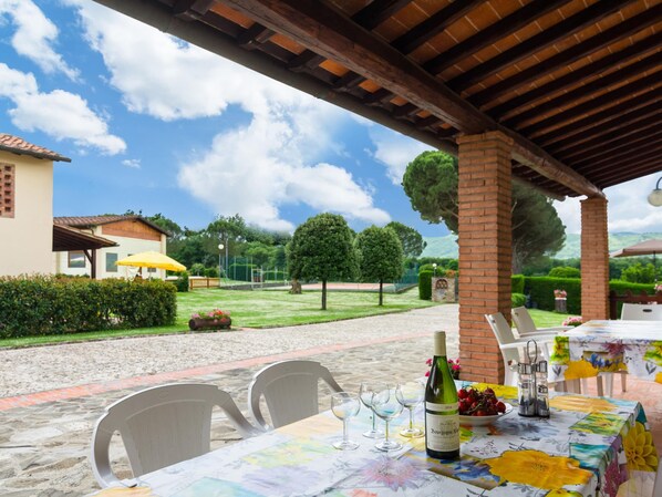 An outdoor dining area with a table set for two, a bottle of wine, and a bowl of fruit. - Farmhouse in Bucine With Pool (Bucine)