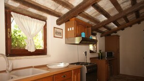 A kitchen with wooden cabinets, a stove, and a window with a curtain. - Belvilla by OYO Appartamento dei Cavalieri (Treia)
