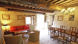 A rustic interior with a stone wall, wooden ceiling beams, a dining table with chairs, a sofa, and a lamp. - Belvilla by OYO Appartamento dei Cavalieri (Treia)