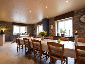 A dining area with a long table, chairs, and a stone wall. - Family Home in Sainte ode (Sainte-Ode)