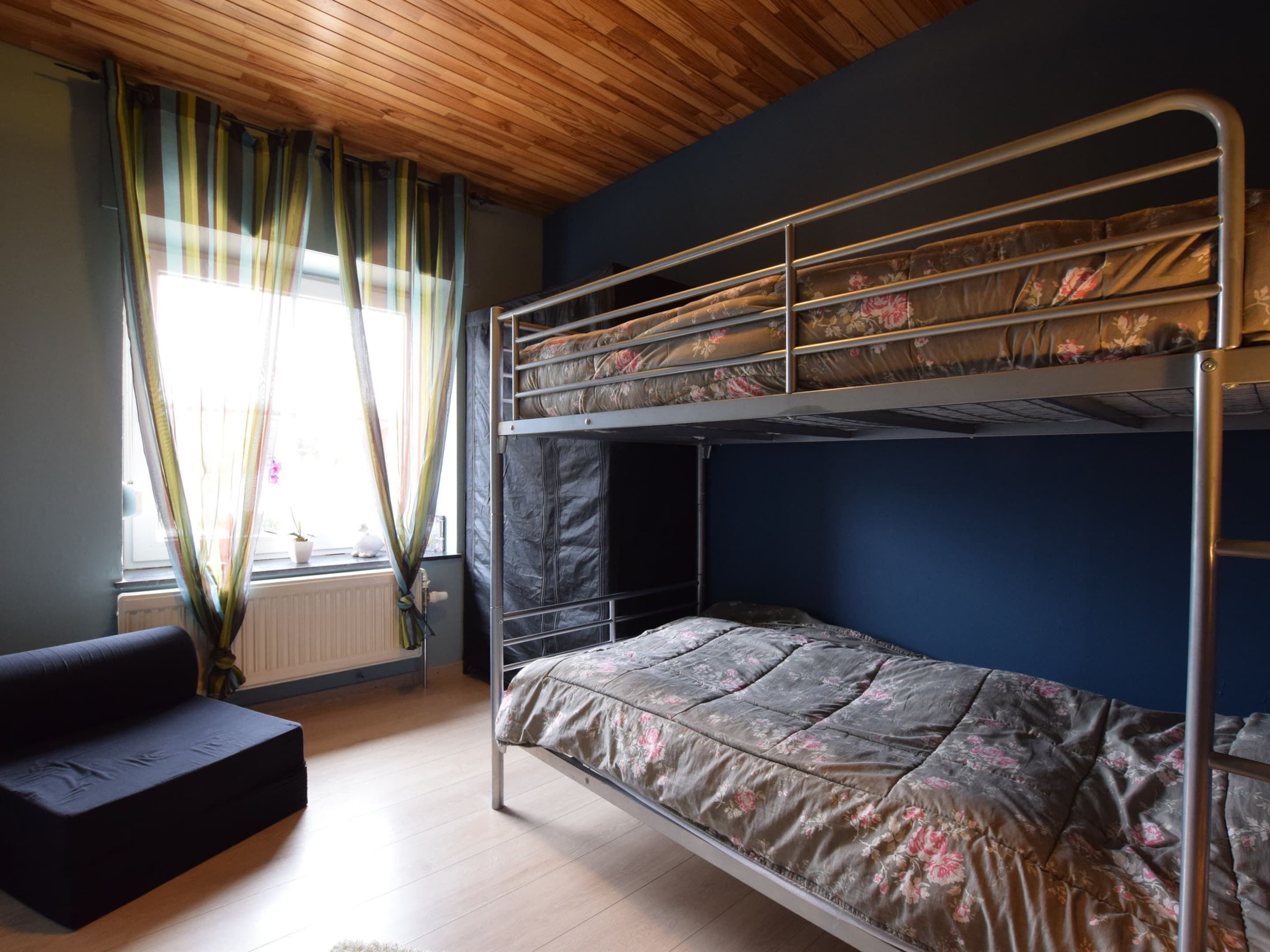 A bunk bed room with a wooden ceiling, a window with curtains, and a black sofa.