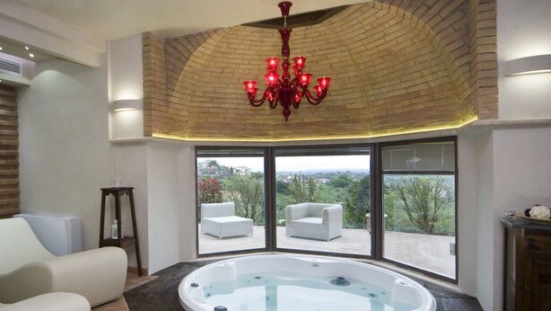 Ein geräumiges Zimmer mit Whirlpool, zwei weißen Sofas, einem Holztisch und einem großen Fenster mit Blick auf Grünflächen und Gebäude.