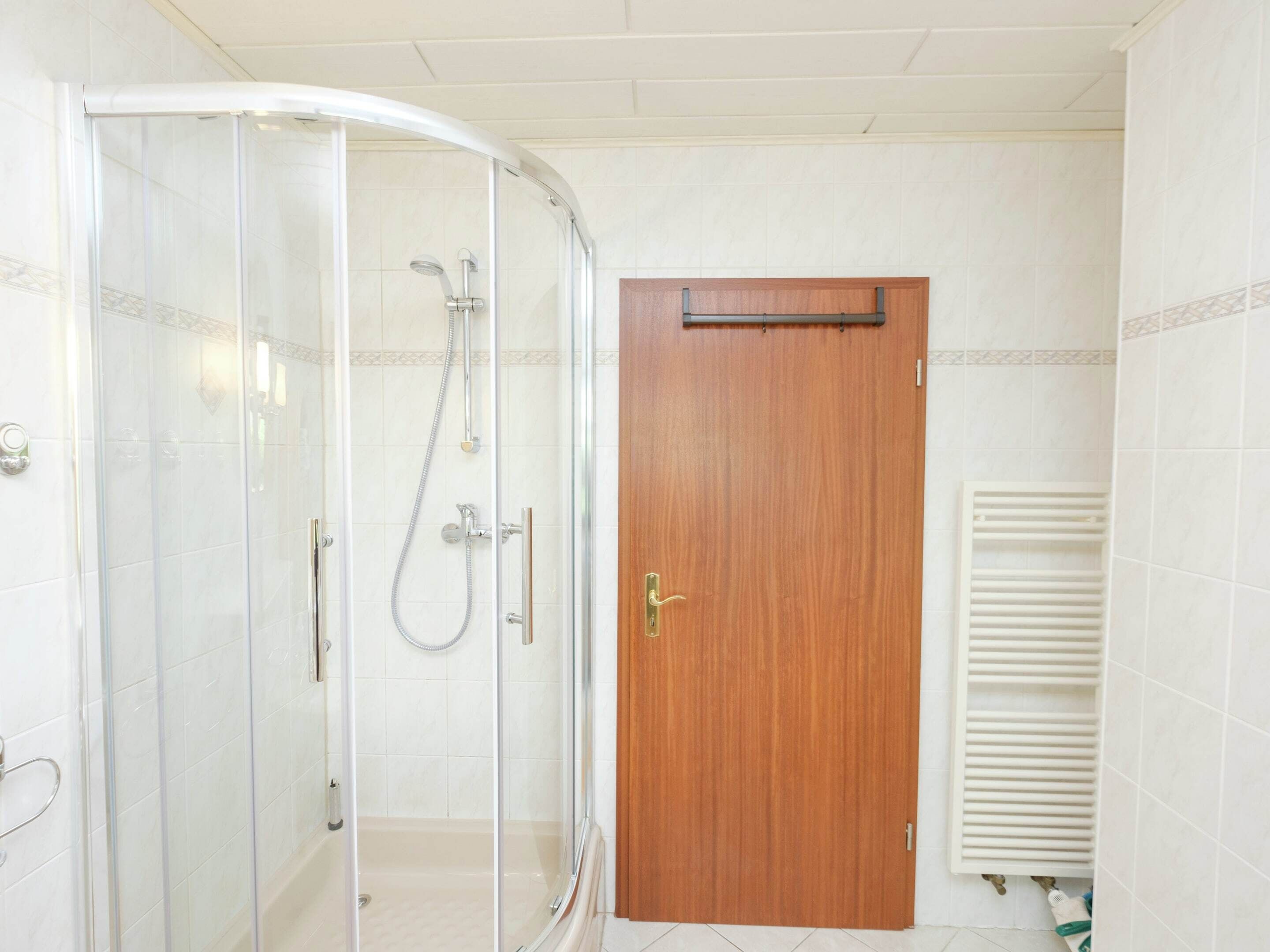 Une salle de bain avec une douche à parois de verre, une porte en bois et un mur recouvert de carreaux blancs.
