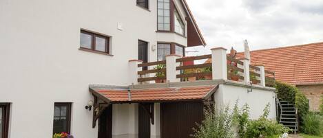 A two-story building with a sloped roof, a wooden balcony, and a stone pathway leading to the entrance.
