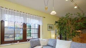 A cozy living room with a sectional sofa, a wooden table, and a large window with lace curtains. - Apartment in Harz With Terrace (Ballenstedt)