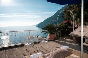 A terrace with a table and chairs, overlooking a body of water and a mountainous coastline. - Chic Hideaway in Positano (Positano)