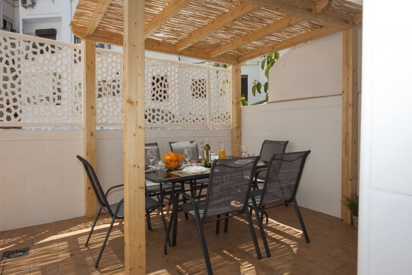 An outdoor patio with a wooden pergola, a dining table set with chairs, and a white fence with decorative cutouts.