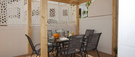 An outdoor patio with a wooden pergola, a dining table set with chairs, and a white fence with decorative cutouts.