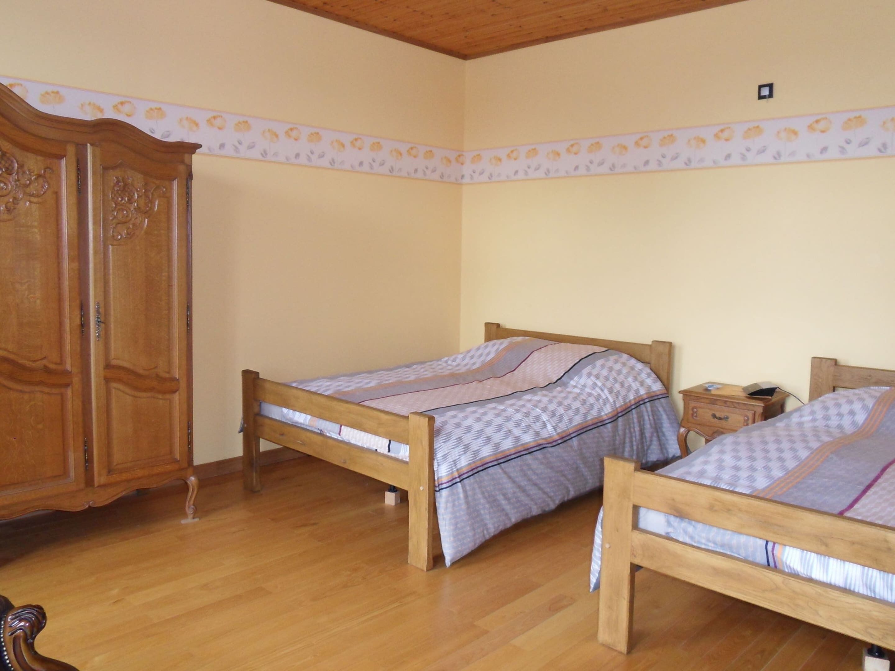A bedroom with two wooden beds, a wooden wardrobe, and a small bedside table with a lamp.