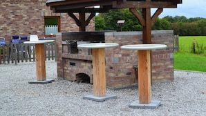 Un espace barbecue extérieur avec un four en briques et des tables en bois.