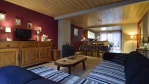 A cozy living room with a wooden ceiling, a television, and a dining area with a table and chairs. - Cottage in Former Farmhouse in Tillet (Sainte-Ode)