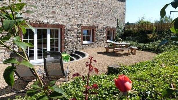 A stone building with a patio area, outdoor seating, and a garden with a red flower. - Cottage in Former Farmhouse in Tillet (Sainte-Ode)