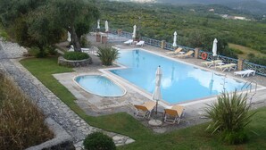 A swimming pool with lounge chairs and umbrellas, surrounded by greenery and mountains in the background. - Villa in Paleokastrites with Swimming Pool near Beaches (Corfu)