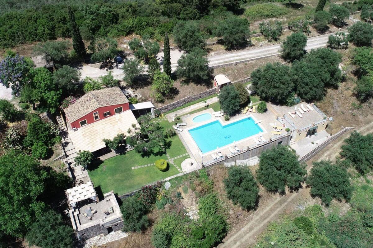 An aerial view of a property with a swimming pool, a red building, and surrounding greenery.