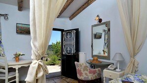 A bedroom with a bed, a chair, a desk, a mirror, and a door leading to an outdoor area. - Villa in Paleokastrites with Swimming Pool near Beaches (Corfu)