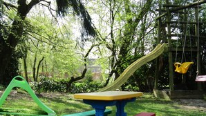 Een speeltuin met een glijbaan, een schommel en een klimrek, gelegen in een grasveld met bomen.