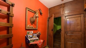 Een kamer met een houten ladder, een lijst met daarop een hertenkop, een boekenkast en een trap naar een andere kamer.