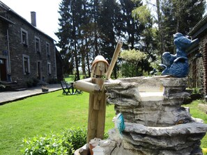 Ein rustikaler Außenbereich mit einer Steinfountain, einer Strohmannfigur und einer blauen Vogel-Skulptur.