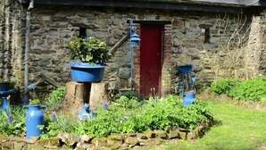Een stenen gebouw met een rode deur, omringd door een tuin met verschillende planten en blauwe potten.