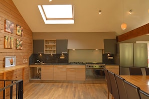 A modern kitchen with wooden cabinets, a skylight, a gas stove, and a dining area with chairs.