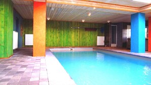 Una piscina interior con techo de madera y paredes pintadas en tonos verde, azul y naranja.