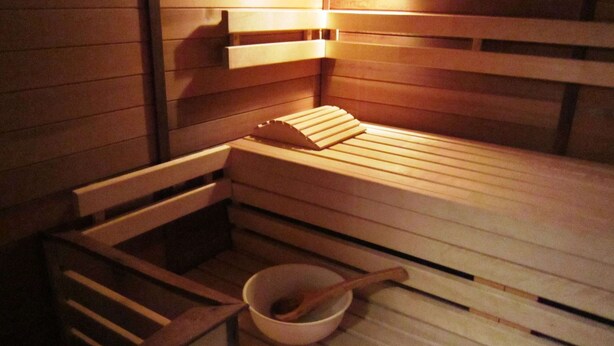 Una sauna con bancos de madera y un tazón de madera con una cuchara de madera.