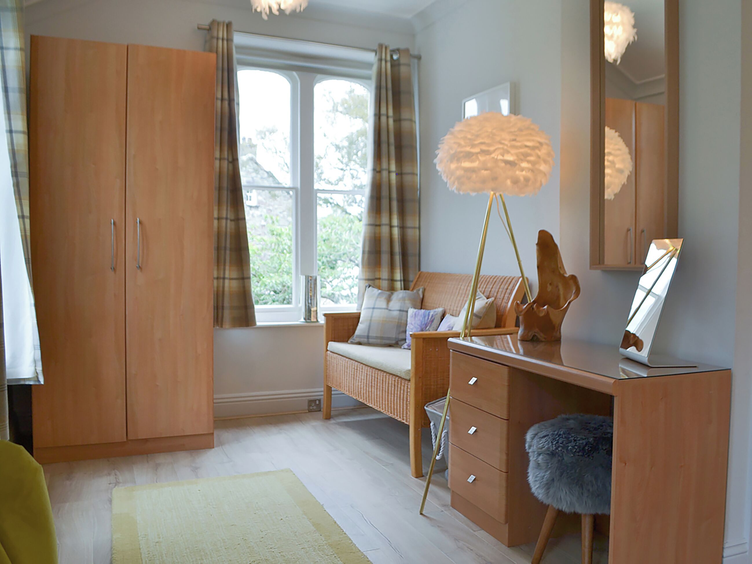 A bedroom with a bed, a dresser, a mirror, a lamp, and a window with curtains.