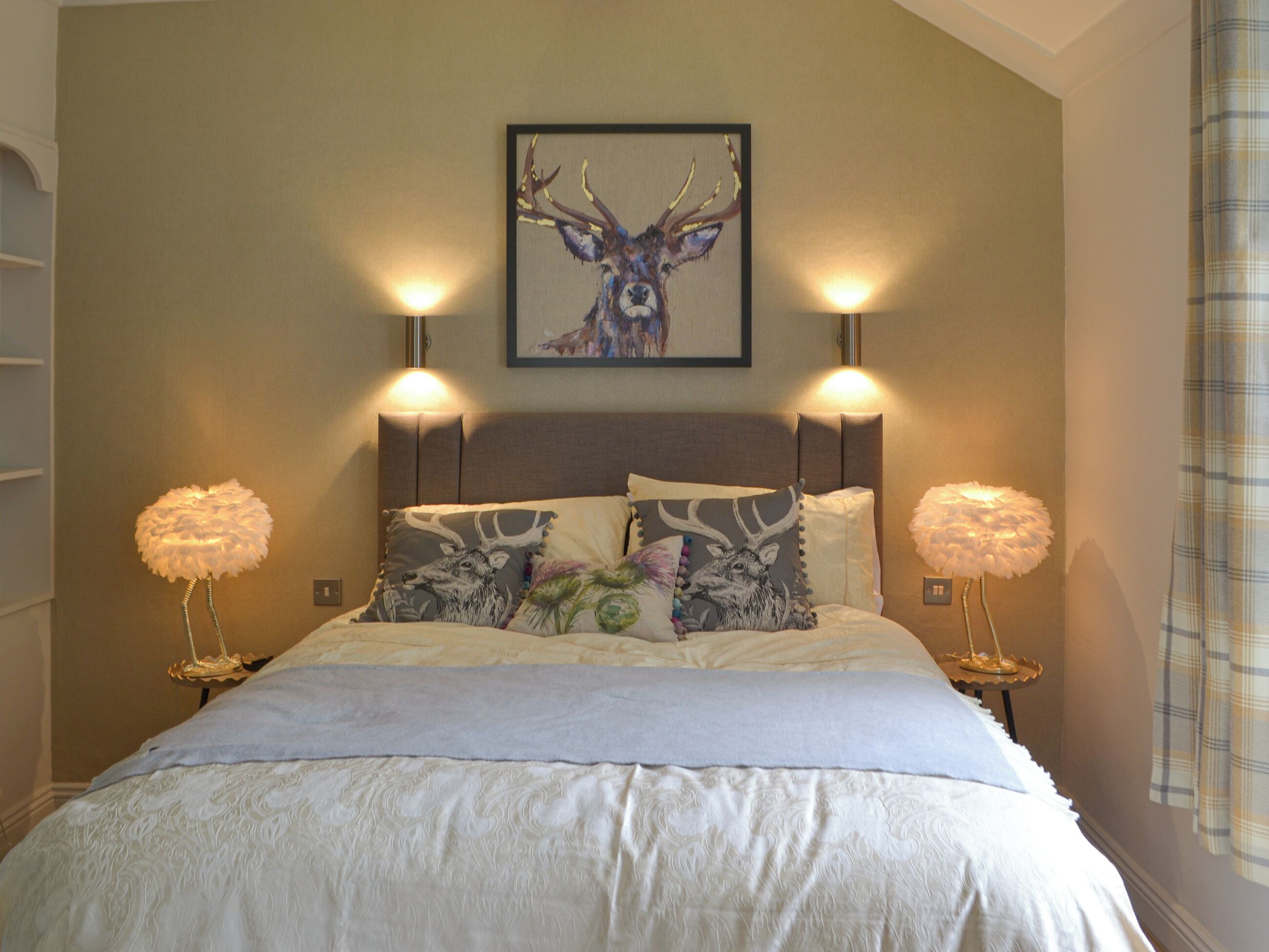 Een slaapkamer met een groot bed, twee wandlampen en een schilderij van een hert.