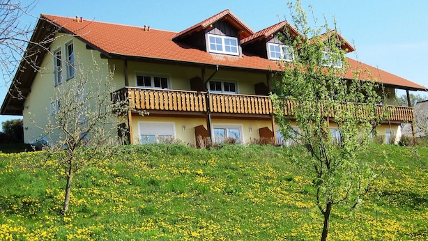 A two-story house with a red-tiled roof, multiple balconies, and a grassy lawn with yellow flowers. - App. in Rotthalmunster Near the spa Triangle (Rotthalmuenster)