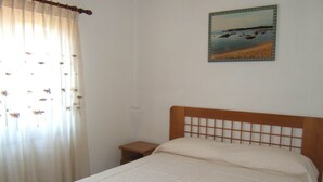 Une chambre à coucher avec un lit, une table de chevet, une fenêtre avec des rideaux et un tableau au mur.