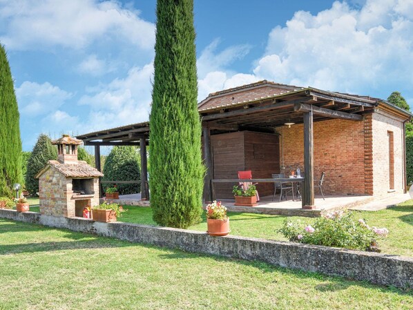 A rustic outdoor patio with a brick barbecue area, a pergola, and potted plants.