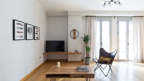 Un salon moderne avec un téléviseur à écran plat, une table basse, une plante en pot, un fauteuil en cuir et une bibliothèque.