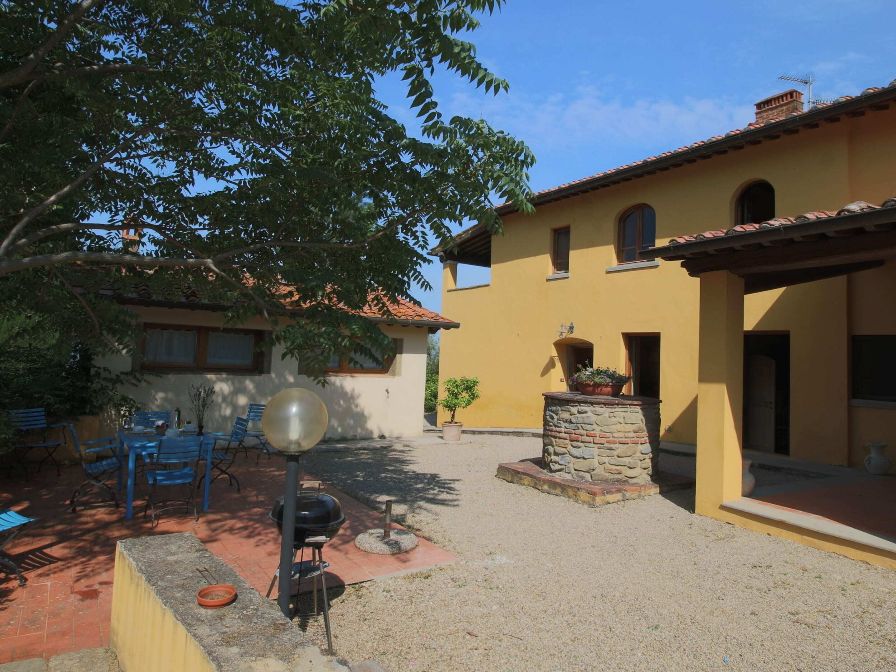 A courtyard with a barbecue grill, outdoor seating, and a yellow building with a tiled roof.