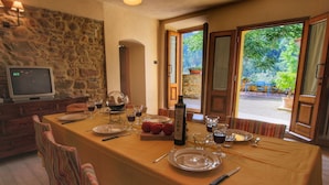 A dining area with a table set for two, a stone wall, and a television in the corner.